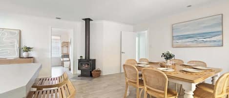 A dining area with a wooden table, wicker chairs, a whiteboard, and a painting of the ocean.
