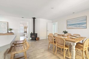 A dining area with a wooden table, wicker chairs, a whiteboard, and a painting of the ocean. - Luna Getaway—Spacious Family Escape by the Coast (Quindalup)