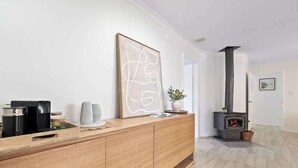 A modern living room with a wooden console table, a large abstract painting, a fireplace, and a view into another room. - Luna Getaway—Spacious Family Escape by the Coast (Quindalup)