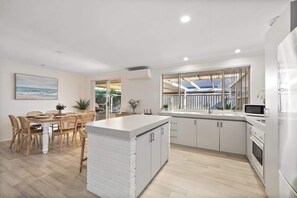 A modern kitchen with white cabinetry, a central island, and a dining area with wooden chairs.
