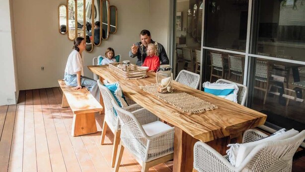 A dining area with a long wooden table, wicker chairs, and a glass partition. - The Bay Retreat (Dunsborough)
