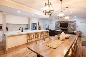 A modern kitchen with a central island, bar stools, a stone accent wall, and a flat-screen TV.