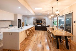 A modern kitchen with a central island, wooden flooring, and a dining area with a long table and chairs.