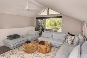 A modern living room with a grey sectional sofa, two wicker ottomans, a patterned rug, and a ceiling fan.