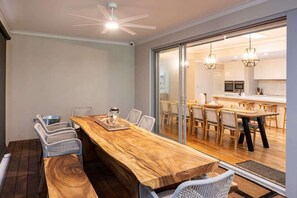 A dining area with a wooden table, wicker chairs, and a view into a kitchen through glass doors.