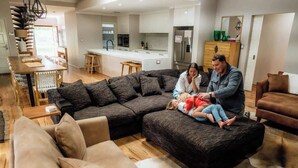 A modern living room with a sectional sofa, a dining area, and a kitchen in the background. - The Bay Retreat (Dunsborough)