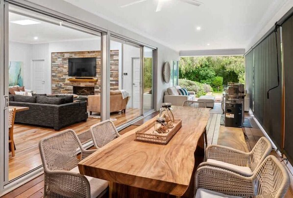 A spacious living area with a wooden dining table, wicker chairs, a fireplace, and a TV.