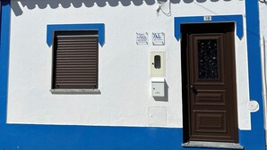 Een gebouw met een blauw-witte gevel, een bruine deur en een raam met een luik.