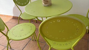 Een aantal groene metalen tafels en stoelen staan op een betegelde vloer, met een rieten mandje op een van de tafels.