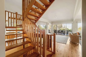 A wooden staircase leading to an upper floor, a dining area with outdoor seating, and large windows providing natural light.