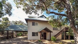 A two-story house with a covered porch, a staircase, and a large tree in the foreground. - Mariners Rest—Bushland Haven w/ Stunning Sea Views (Eagle Bay)