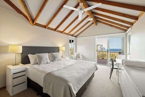 A bedroom with a bed, bedside tables, a ceiling fan, and a balcony with a view.