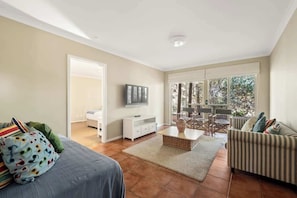A spacious living room with a sofa, a television, a dining area, and a large window.
