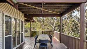 A covered outdoor deck with a wooden table and chairs, surrounded by a railing. - Mariners Rest—Bushland Haven w/ Stunning Sea Views (Eagle Bay)