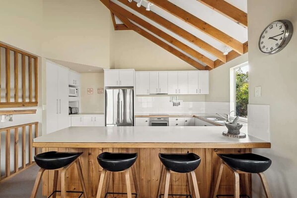 A modern kitchen with white cabinets, a stainless steel refrigerator, and a wooden island with bar stools.