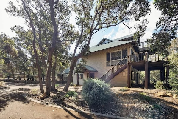 A two-story house with a balcony, surrounded by trees and a driveway.