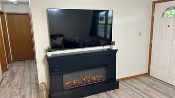 A modern living room with a flat-screen TV mounted above a black fireplace, wooden flooring, and a white door.