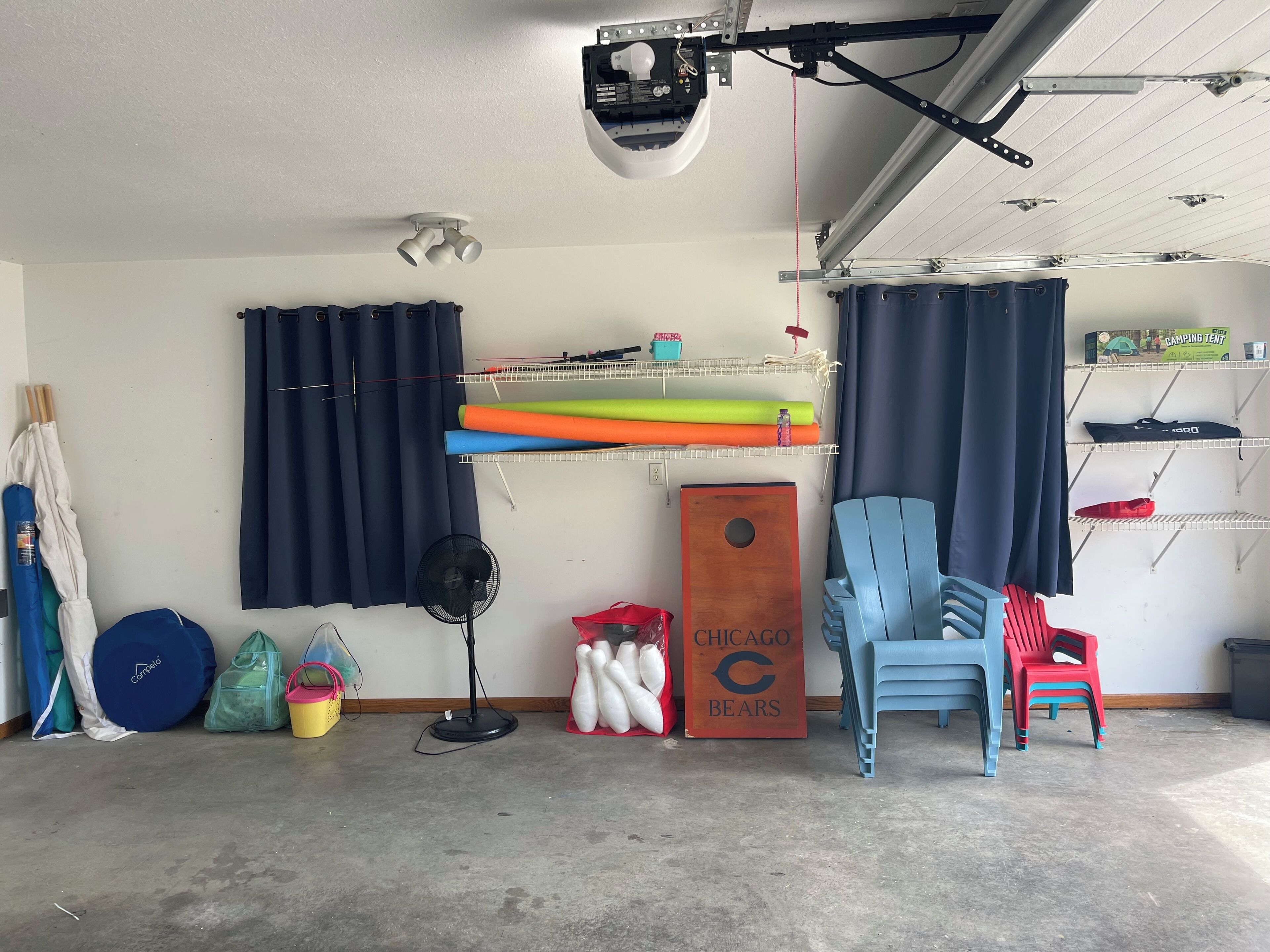 A garage with a ceiling fan, a storage rack with mats, a wooden door with a logo, and a blue chair.