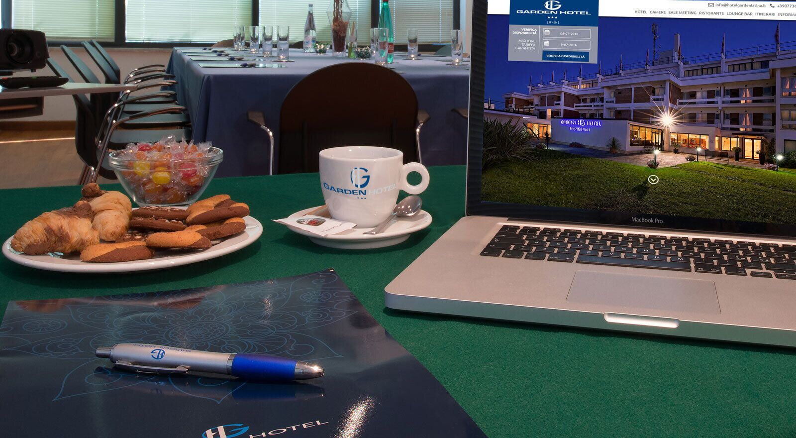 Ein Hotelzimmer mit einem Laptop, einer Auswahl an Gebäck, einer Tasse und einem Stift auf einem grünen Tisch.