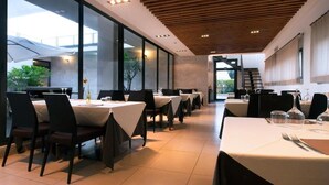 Un espace repas moderne, doté de tables et de chaises, de grandes fenêtres et d’un plafond en bois.