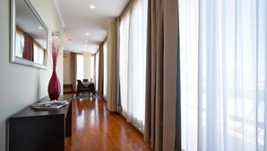 Un couloir d’hôtel avec un plancher en bois, un comptoir de réception, un espace repas et de grandes fenêtres avec des rideaux.