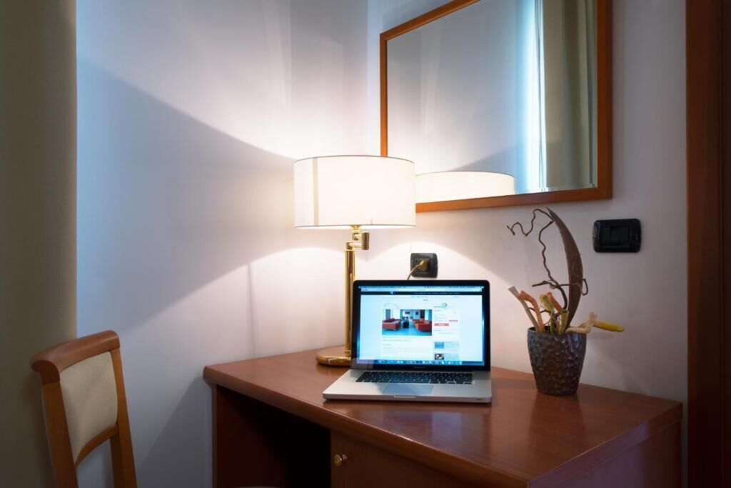 A laptop on a wooden desk with a lamp, a mirror, and a potted plant.
