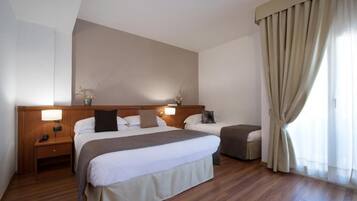 Une chambre d’hôtel avec deux lits, un plancher en bois, une grande fenêtre avec des rideaux et un luminaire fixé au mur.