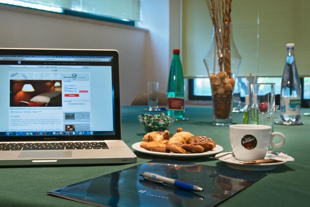 A laptop on a table with a glass of water, a cup of coffee, and a plate of pastries.