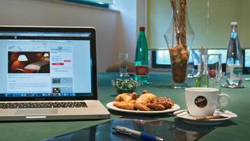 A laptop on a table with a glass of water, a cup of coffee, and a plate of pastries.