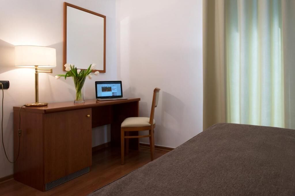 Habitación de hotel con un escritorio de madera, una computadora portátil, una silla, una cama y una ventana con cortinas.