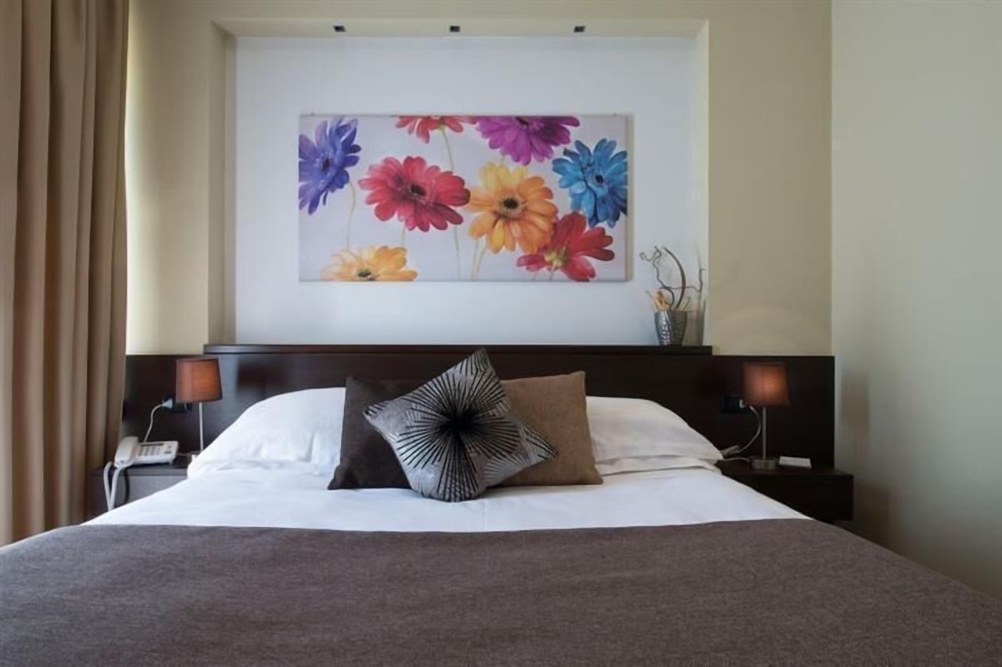 Una habitación de hotel con una cama grande, dos lámparas de noche, un teléfono y una obra de arte floral en la pared.