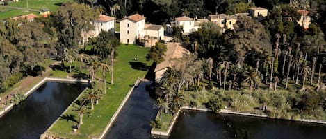 An aerial view of a property with multiple buildings, a large central courtyard, and surrounding water bodies.