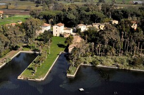 An aerial view of a property with multiple buildings, a large central courtyard, and surrounding water bodies. - HOTEL GARDEN (Latina)