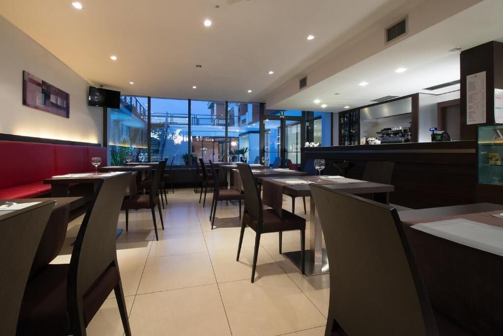 Un restaurante moderno con mesas y sillas altas, una zona de bar y grandes ventanales que ofrecen vistas al exterior.
