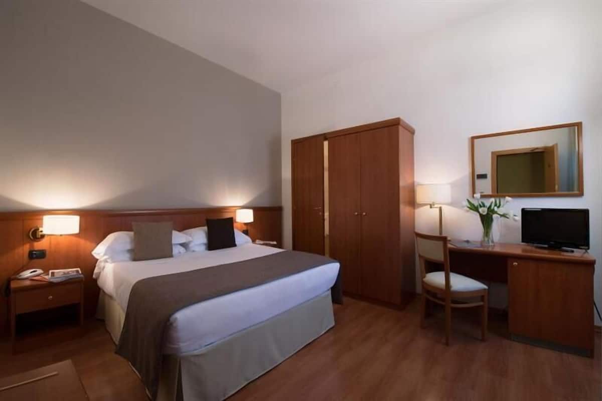 A hotel room with a bed, a desk, a chair, a TV, a wardrobe, and a mirror.