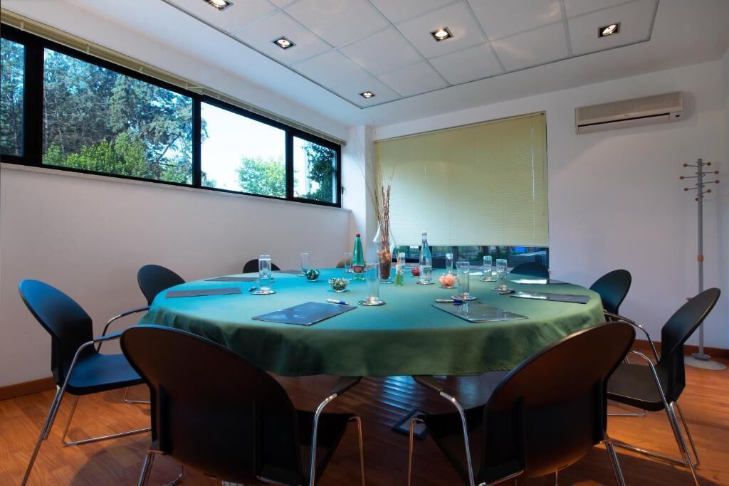 A conference room with a round table, black chairs, a green tablecloth, and a window with blinds.