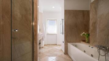 A modern bathroom with a large bathtub, a glass shower enclosure, and a marble floor.