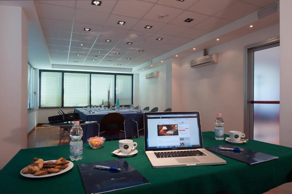 Una sala de conferencias con una mesa verde, computadoras portátiles, botellas de agua y un plato de pasteles.