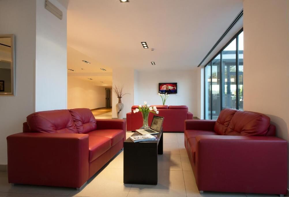 A modern living room with red leather sofas, a black coffee table, and a flat-screen TV mounted on the wall.
