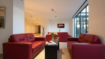 A modern living room with red leather sofas, a black coffee table, and a flat-screen TV mounted on the wall.