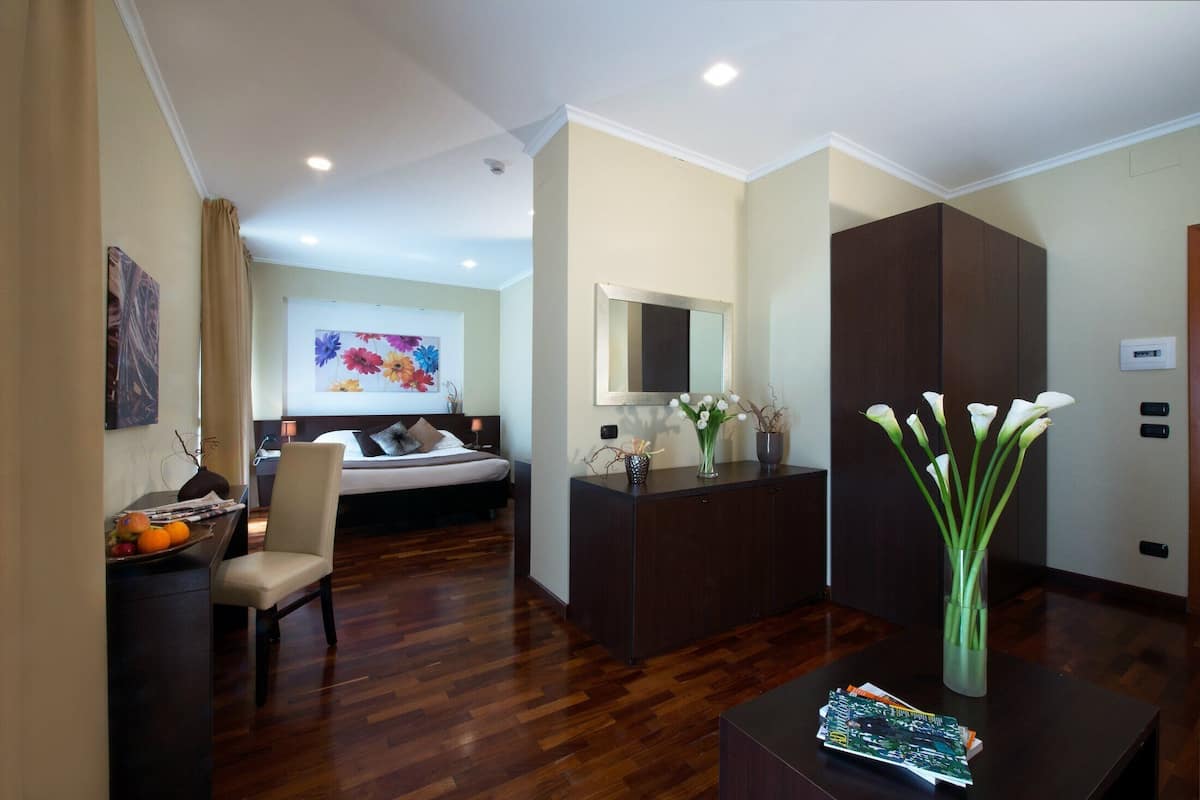 A hotel room with a bed, a desk with a chair, a vase with flowers, and a magazine on the table.