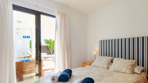 Hotelkamer met een bed, nachtkastje met lamp, schuifdeur naar een buitenruimte en uitzicht op groen.