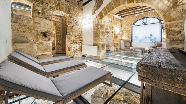 Un espacio de spa con paredes de piedra, sillas reclinables, piso de vidrio y un banco de piedra.