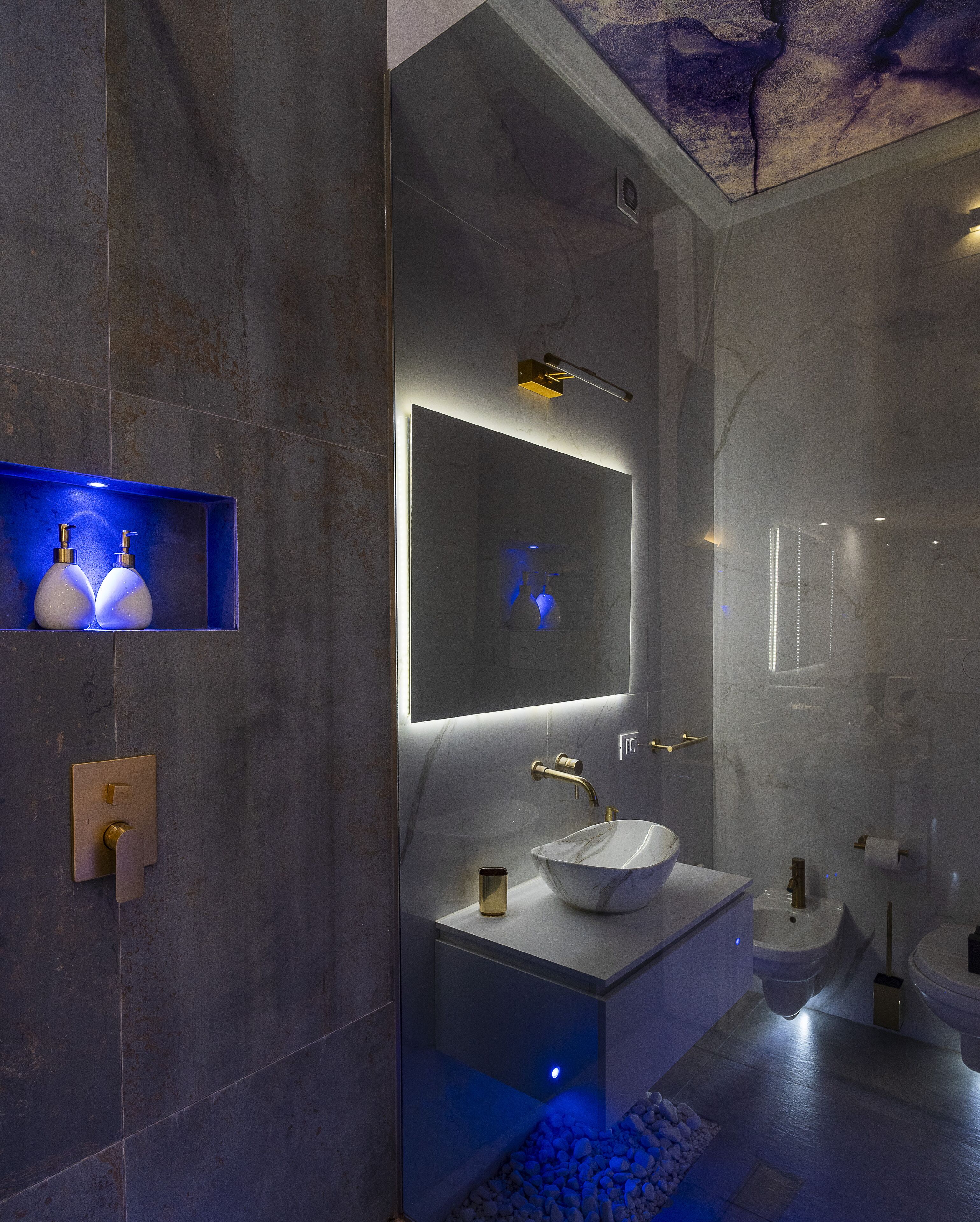 Ein modernes Badezimmer mit einem мраморбеn Waschbecken, einem großen Spiegel und einem blauen Regal mit zwei Flaschen.