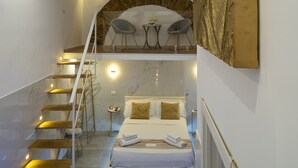 Una habitación de hotel moderna con una escalera de mármol, una cama con dos almohadas, una mesita con sillas y una obra de arte en la pared.