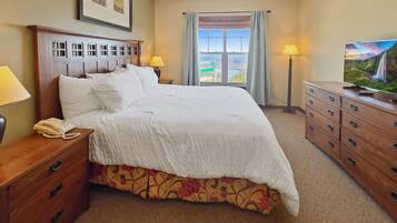 A hotel room with a large bed, bedside lamps, a wooden dresser, a telephone, and a television.
