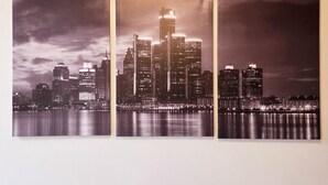 Three black and white photographs of a city skyline at night, displayed on a wall. - Spacious Loft w/ Riverfront Views & Comfort! (Detroit)