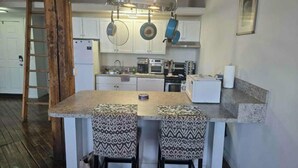 A kitchen with white cabinets, a central island with two patterned stools, hanging pots, and a ladder. - Spacious Loft w/ Riverfront Views & Comfort! (Detroit)