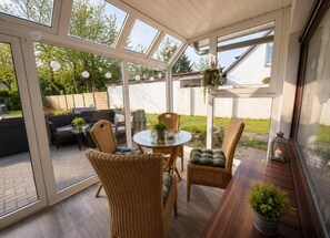 A sunlit patio with wicker furniture, a glass table, and a hanging planter. - Fewo Nina, Am Swatten Diek 4, 27476 Cuxhaven Sahlenburg (Cuxhaven-Sahlenburg)