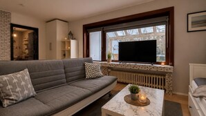 A modern living room with a sofa, a TV, a coffee table, and a window with a view.